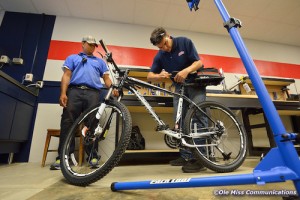 Ole Miss Bike Shop mechanic Stephen Valliant tightens the rear bag mount on one of several new bicycles to be used by Ole Miss Parking and Transportation staff as Traffic Officer Emanuel McJunkins looks on. Photo by Robert Jordan/Ole Miss Communications
